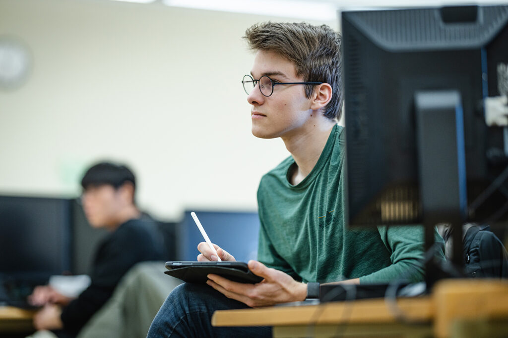 Student sitting next to a desktop, taking notes