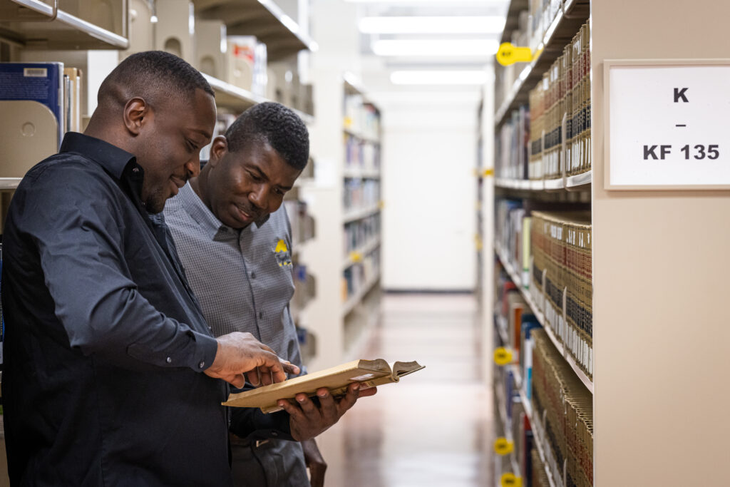 Two men looking at a book in a library