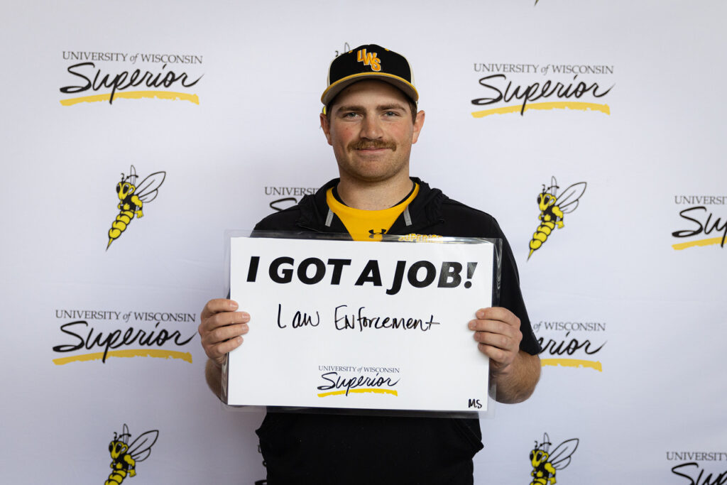 A photo of a student holding a sign that says that he got a job in law enforcement.