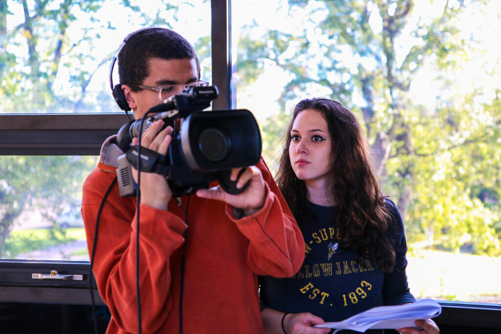 One student holding a video camera and another standing next to him