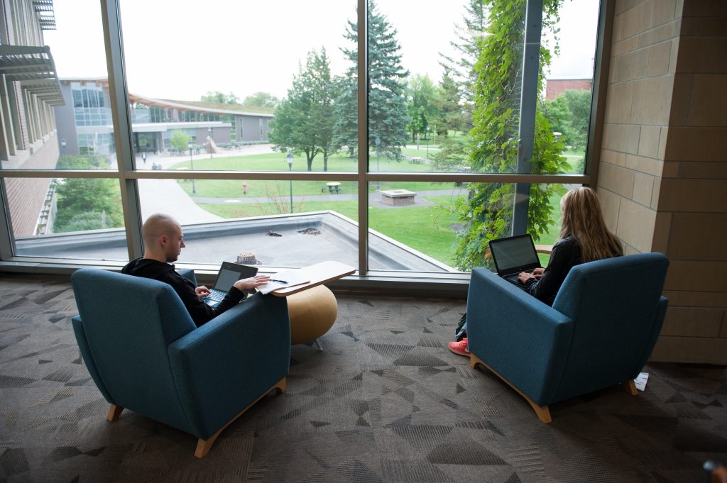 Two students working in front of window overlooking green campus