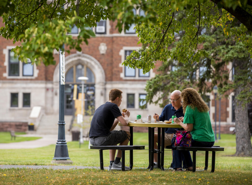 A student eating with his parents at a picnic table